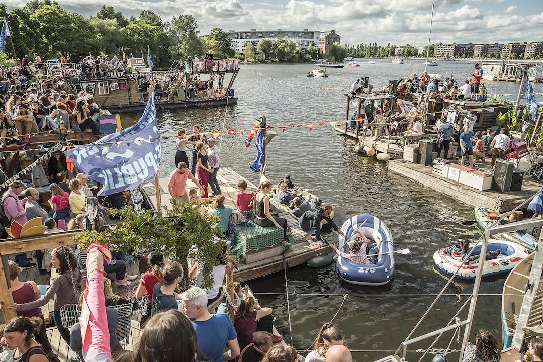 Menschen auf Flößen und Booten auf dem Rummelsburger See, die einer Musik-Band zuhören